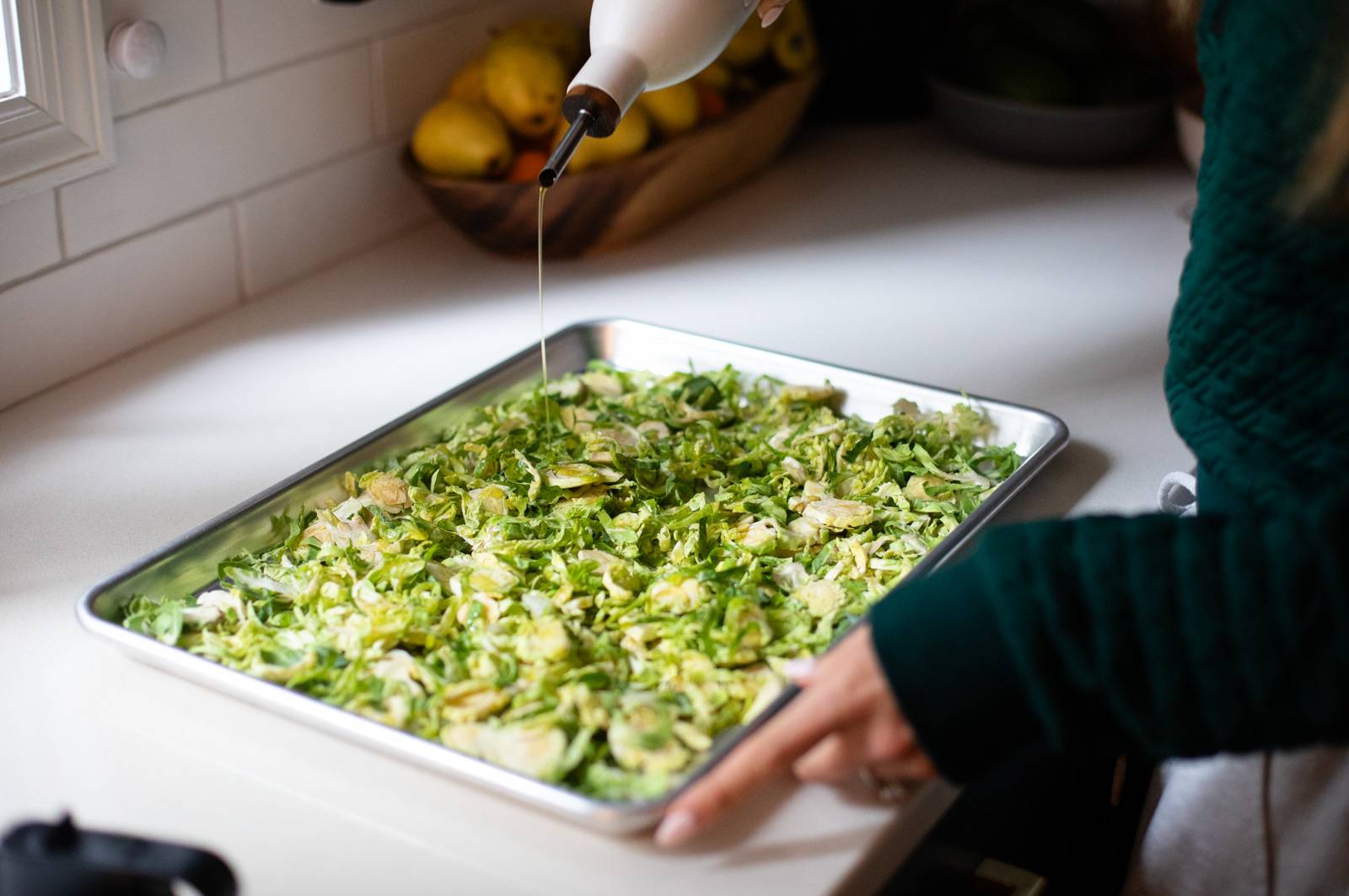 Drizzling oil on shredded brussels sprouts on a sheet pan.