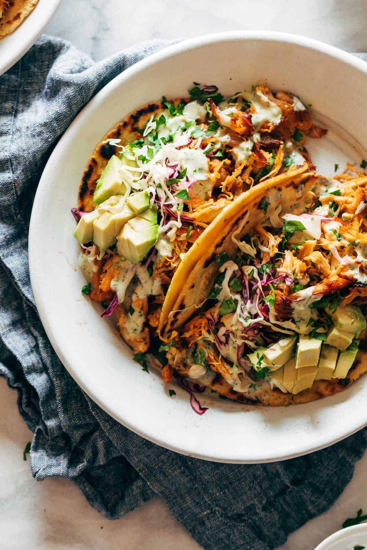 Buffalo chicken tacos on a plate with avocado and slaw.