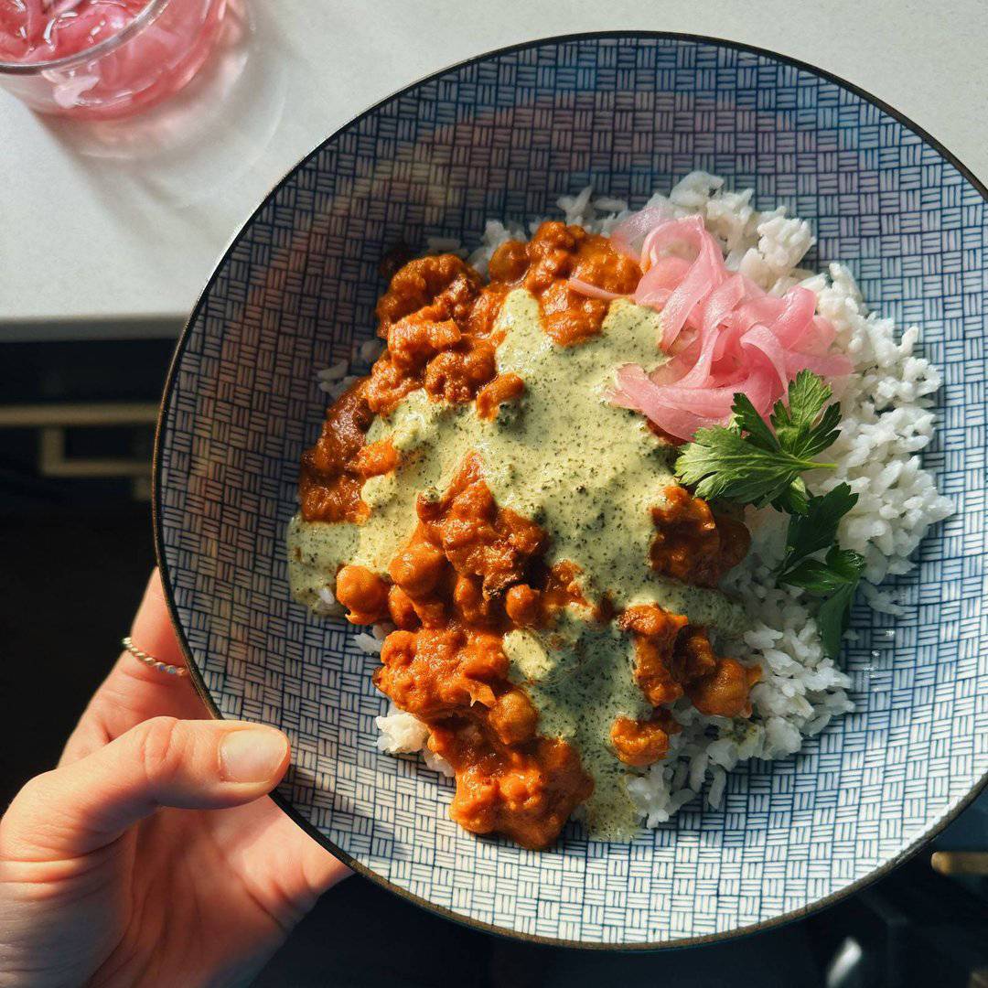 Butter cauliflower and chickpeas in a bowl with rice, pickled onions, and mint cilantro sauce.