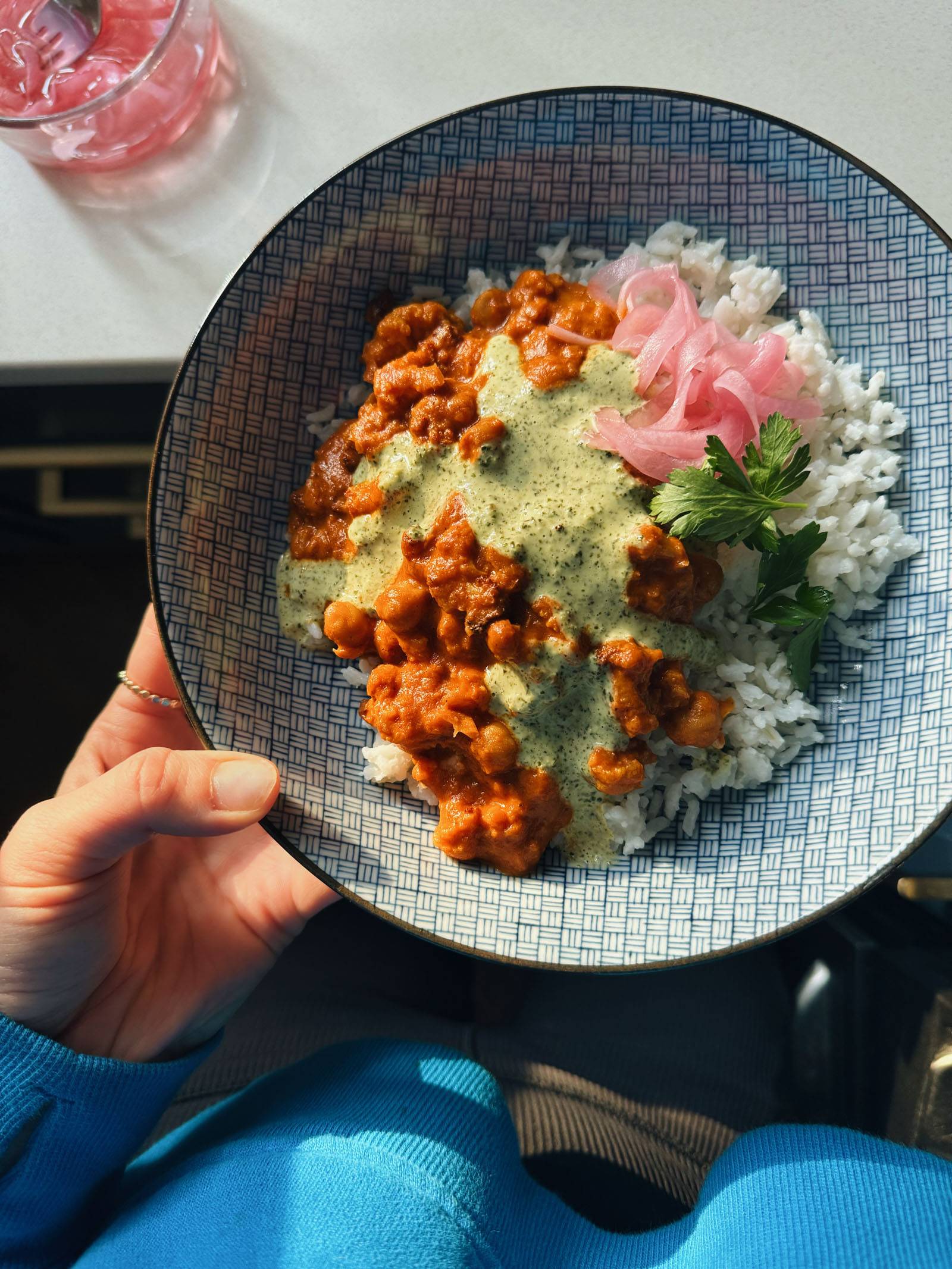 Butter cauliflower and chickpeas in a bowl with rice, mint sauce, cilantro, and pickled onions.