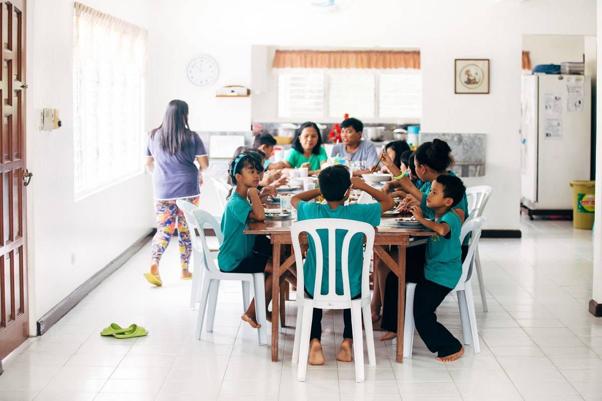 Multiple children and adults sitting at a kitchen table.