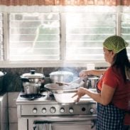 A woman cooking at a stove with a green hair net.