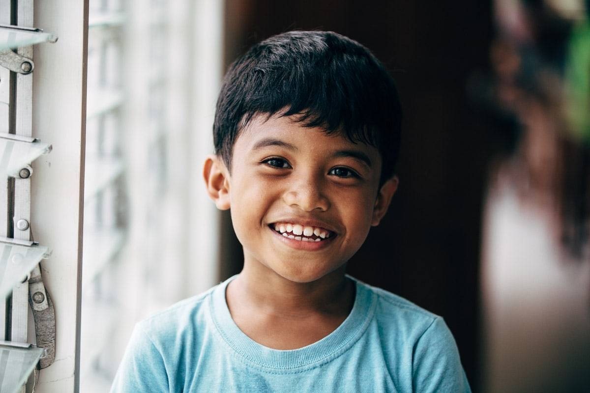 Young boy smiling at camera wearing a blue shirt.