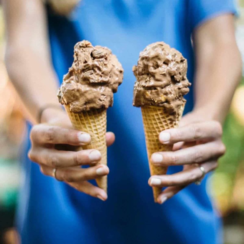 Person holding two chocolate ice cream cones.