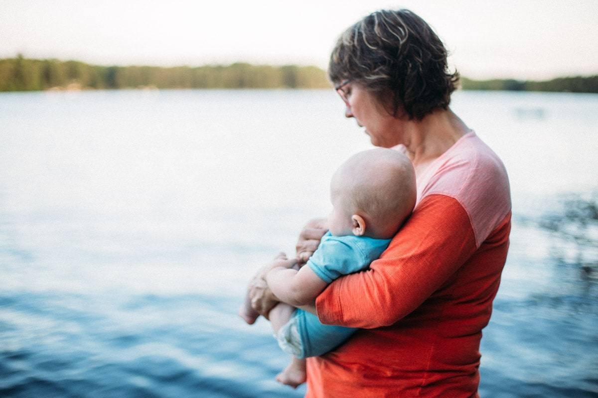 Woman holding a baby looking at the lake.