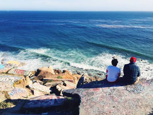 Two people sitting on rocks looking at the ocean.