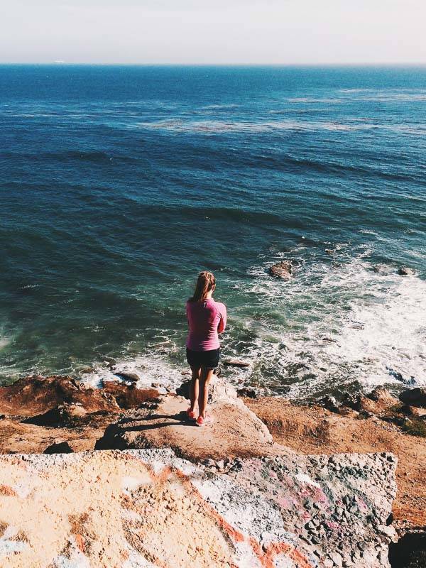 Woman standing on rocks near the ocean.