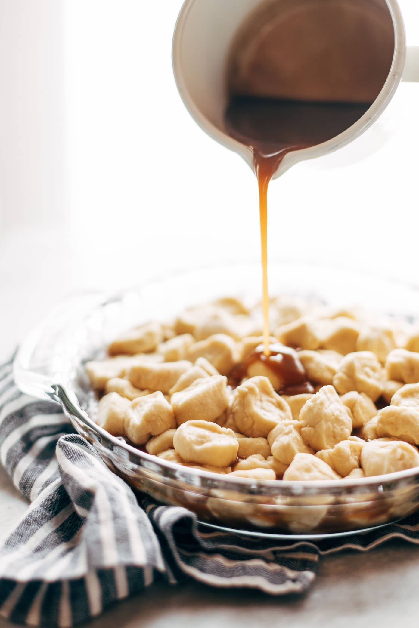 A bowl filled with Monkey Bread and caramel is being spread over it.