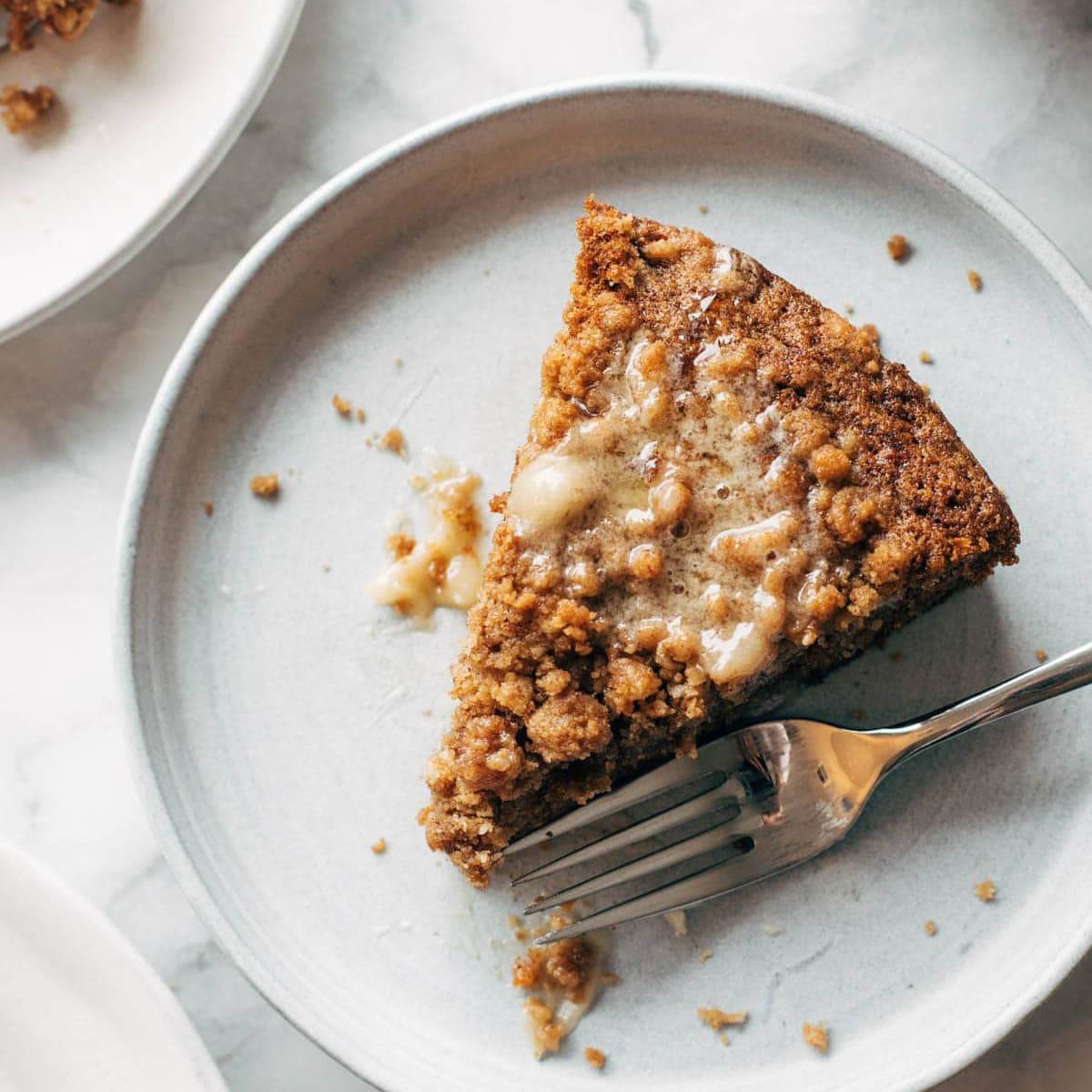 A slice of carrot coffee cake with honey butter on a plate with a fork.
