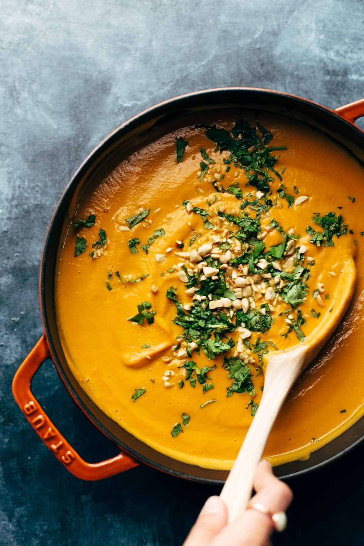 Spicy Vegan Carrot Soup in a pan with a wooden spoon