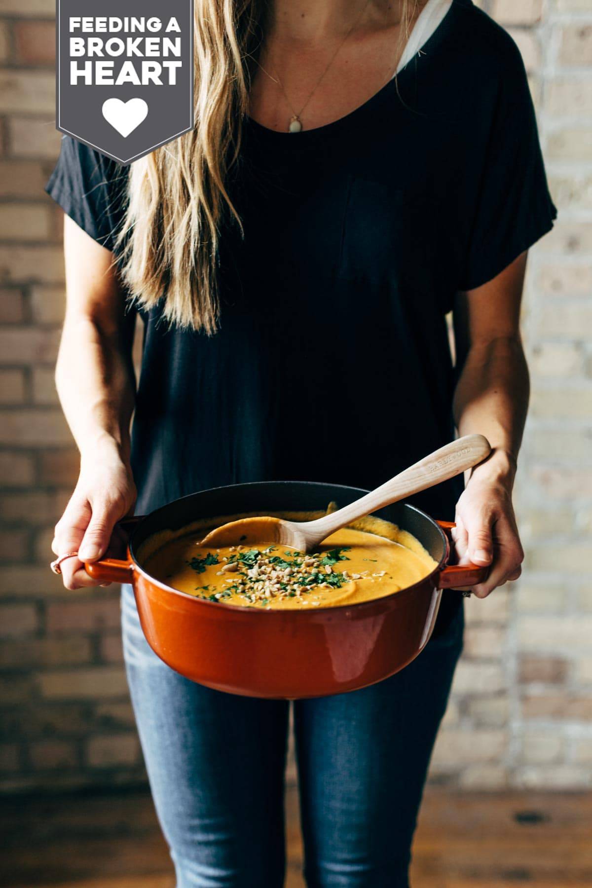 Woman holding a pot of Spicy Vegan Carrot Soup 