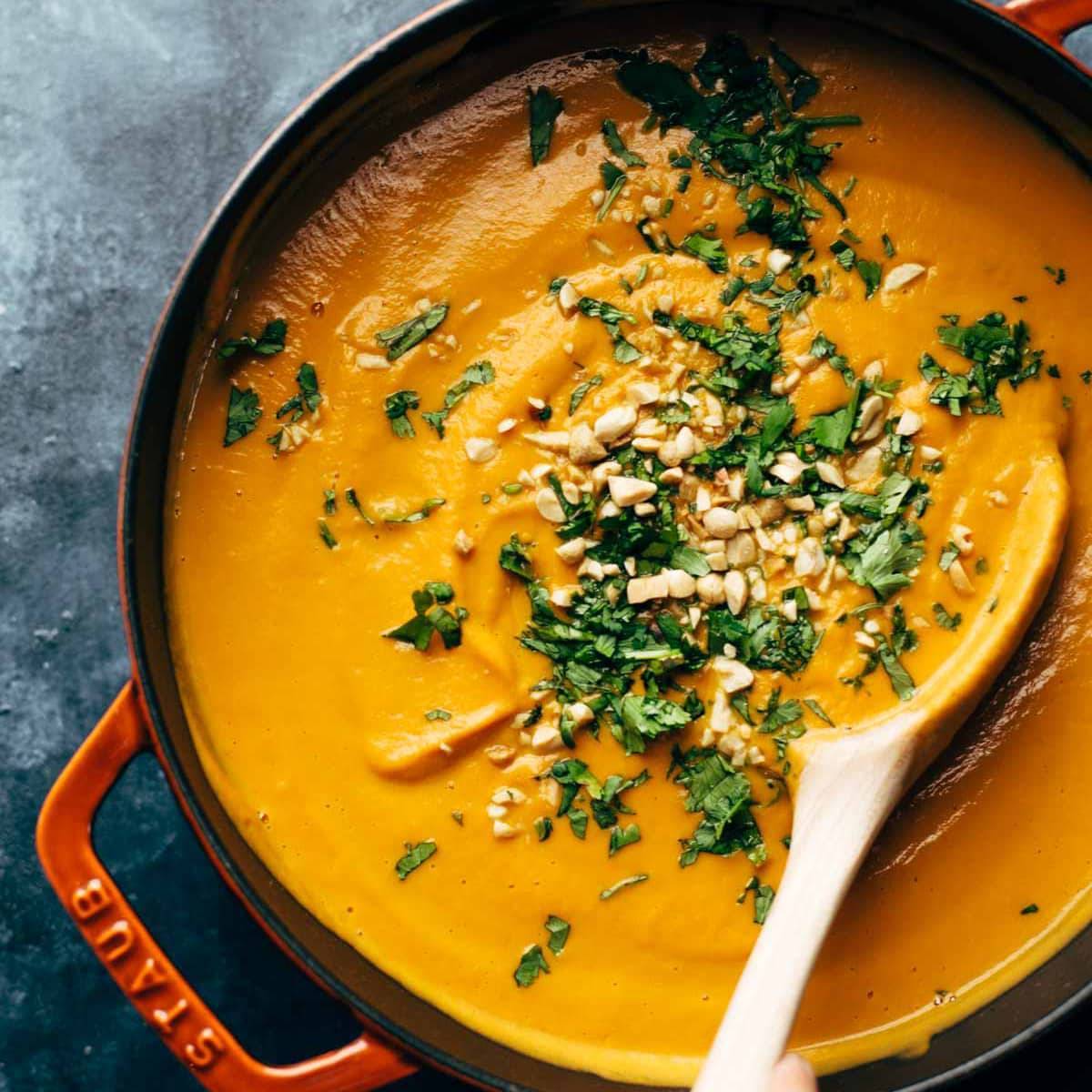 Spicy Carrot Soup in pot with wooden spoon.