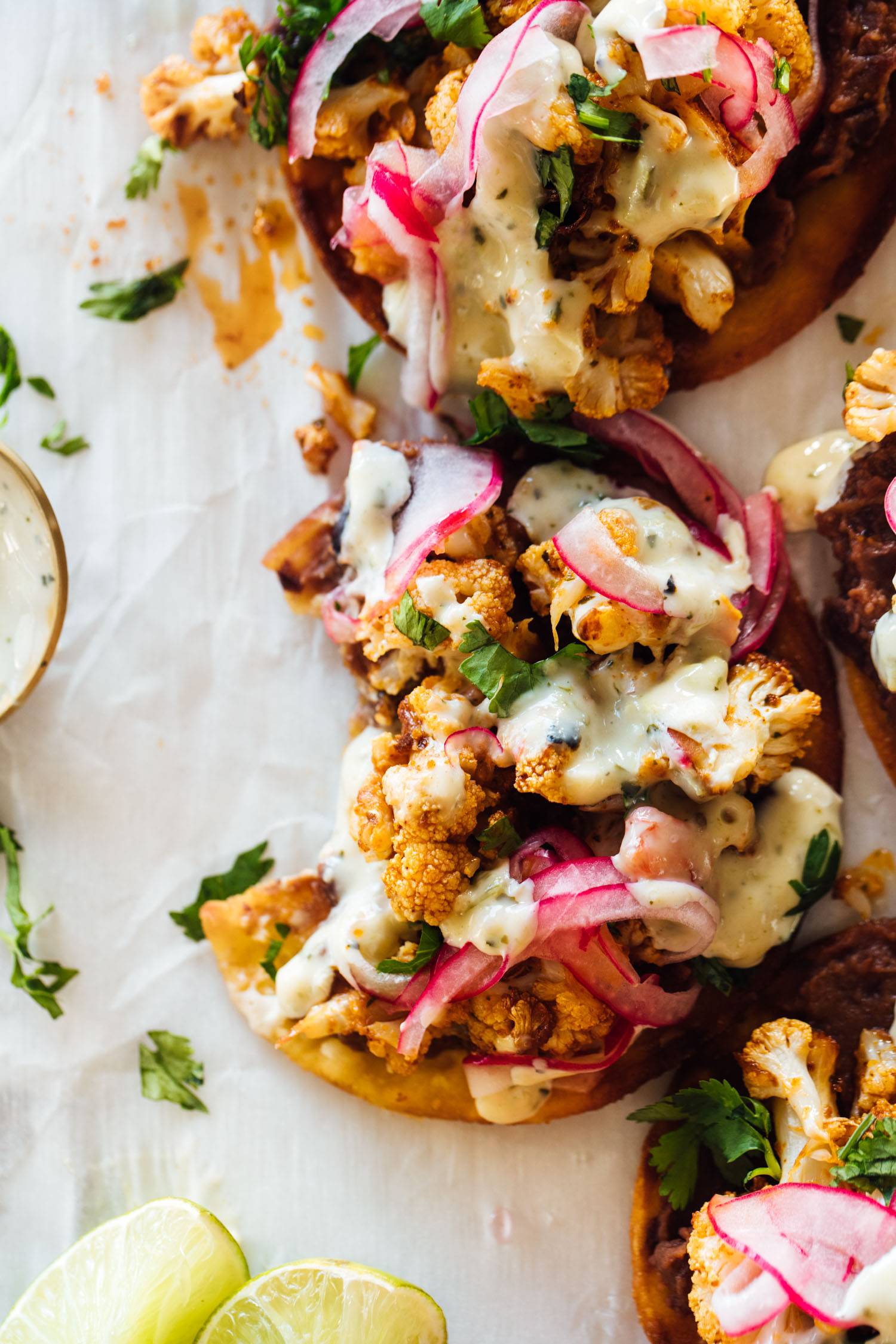 Cauliflower black bean tostadas on parchment paper with pickled onions and queso.