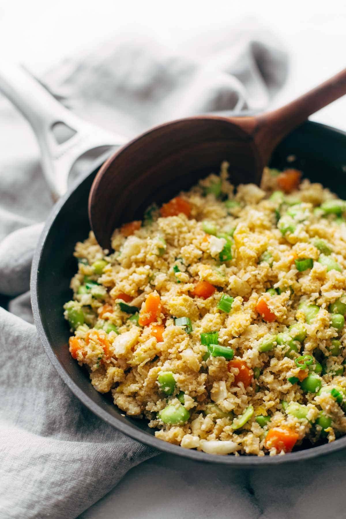 cauliflower fried rice in a pan with a wooden spoon on a napkin