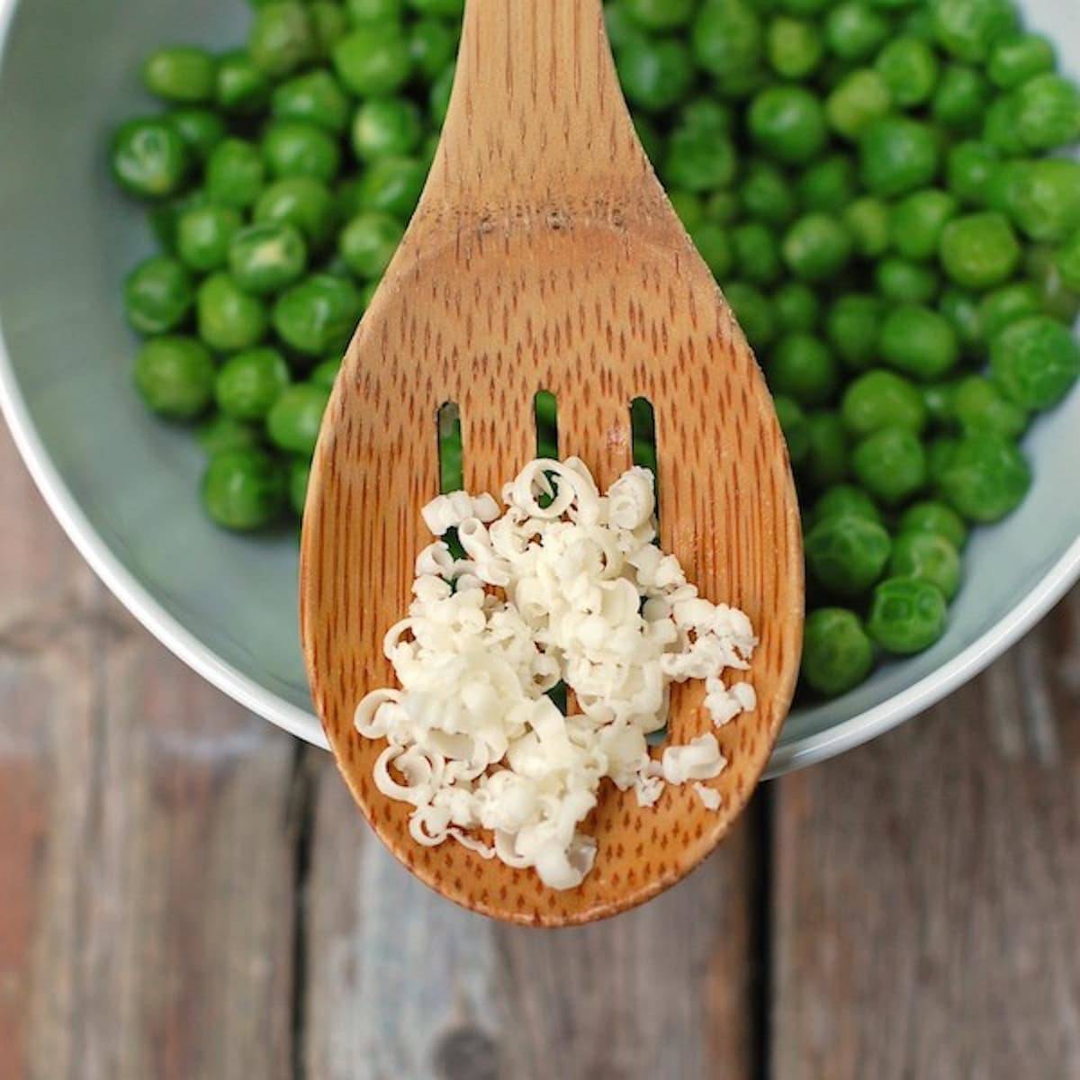 Cheese on a wooden spoon on top of a bowl of peas.