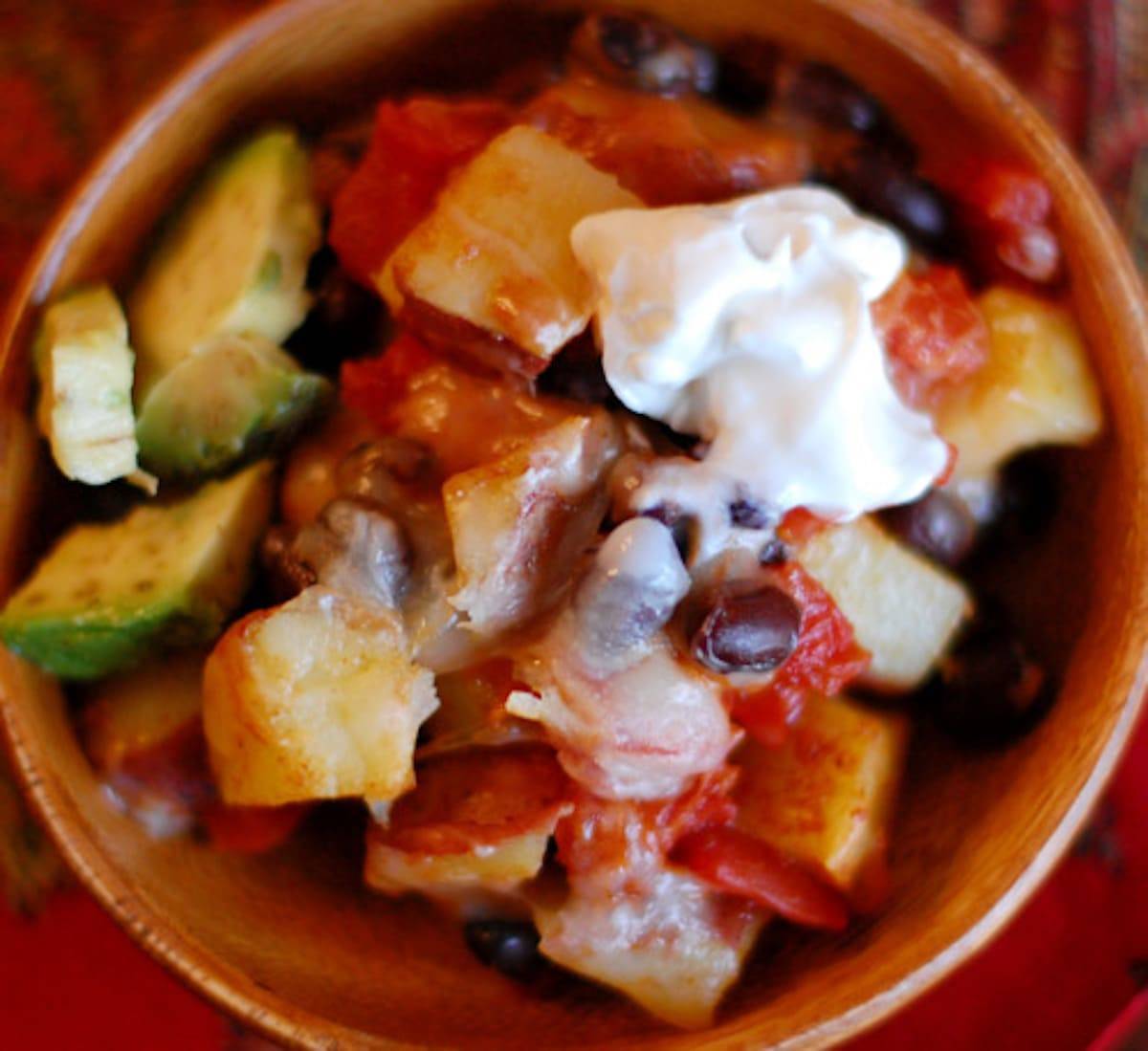 Cheesy roasted potato nachos in a wooden bowl with sour cream topping.