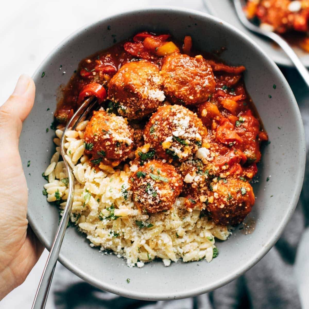 Crispy chicken meatballs, pepper and orzo in a bowl with fork.