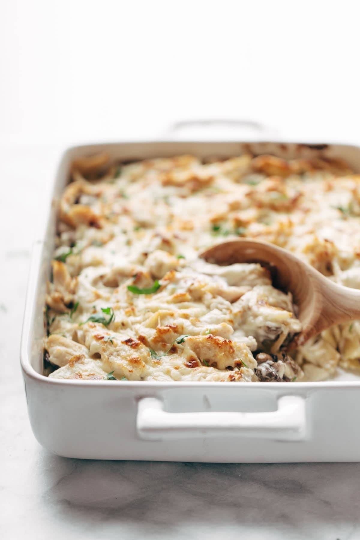 Chicken Tetrazzini in a pan with a wooden spoon.