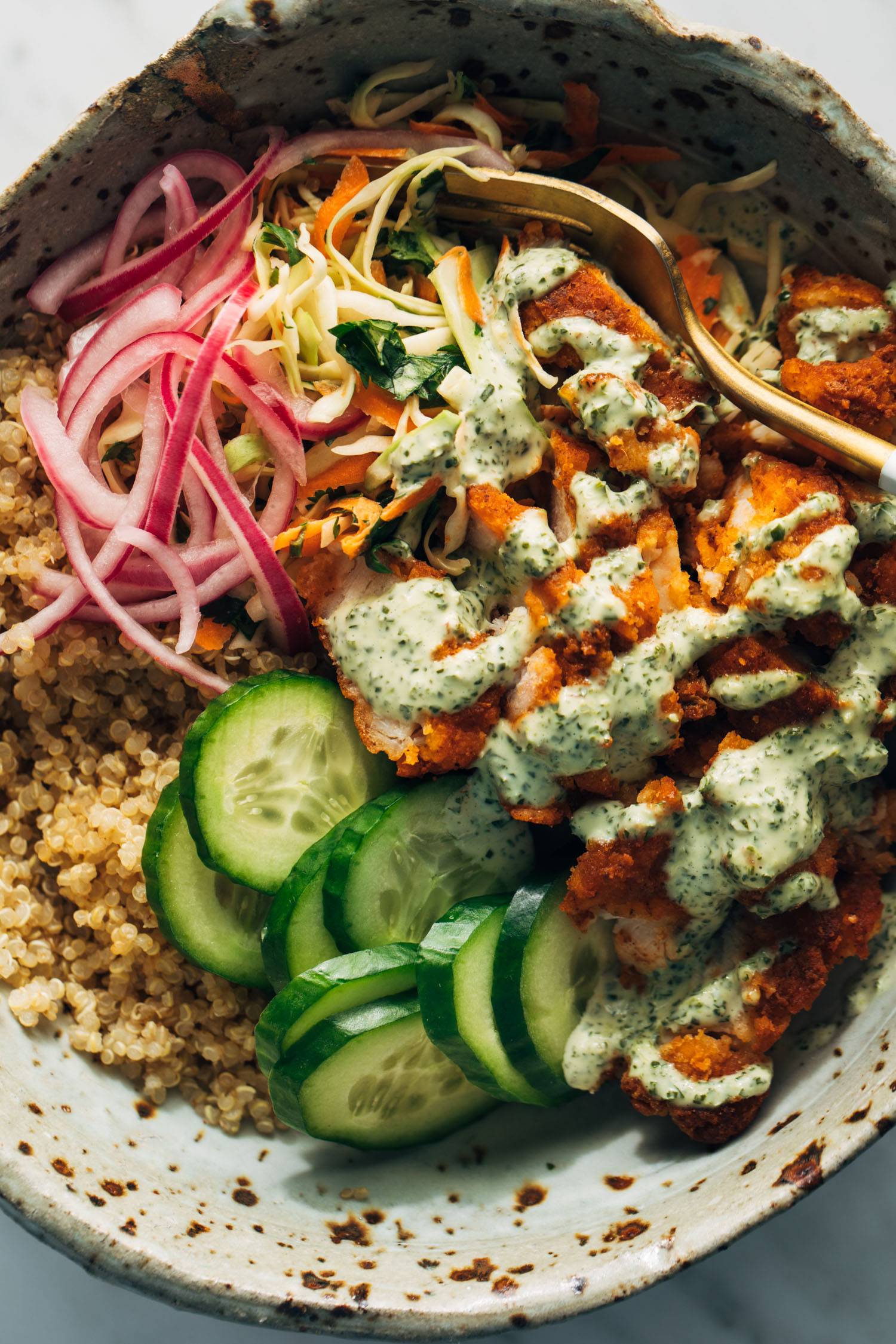 Crispy chicken, quinoa, cucumber ու pickled onion in mint sauce ամ in a bowl with a fork