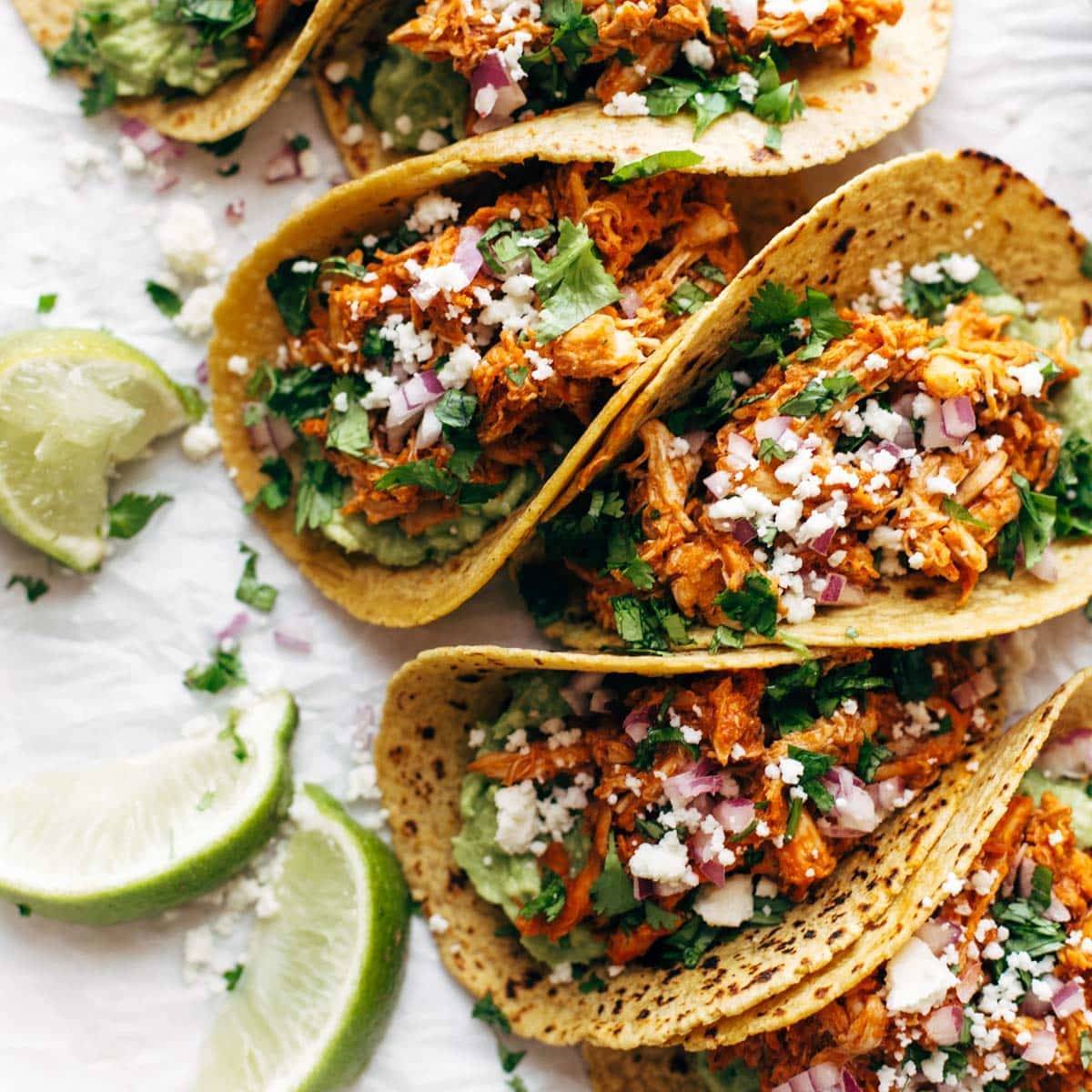 Spicy, saucy Chicken Tinga Tacos with fire-roasted tomatoes, smoky chipotle, garlic, chopped onions, corn tortillas and a lime wedge for squeezing.