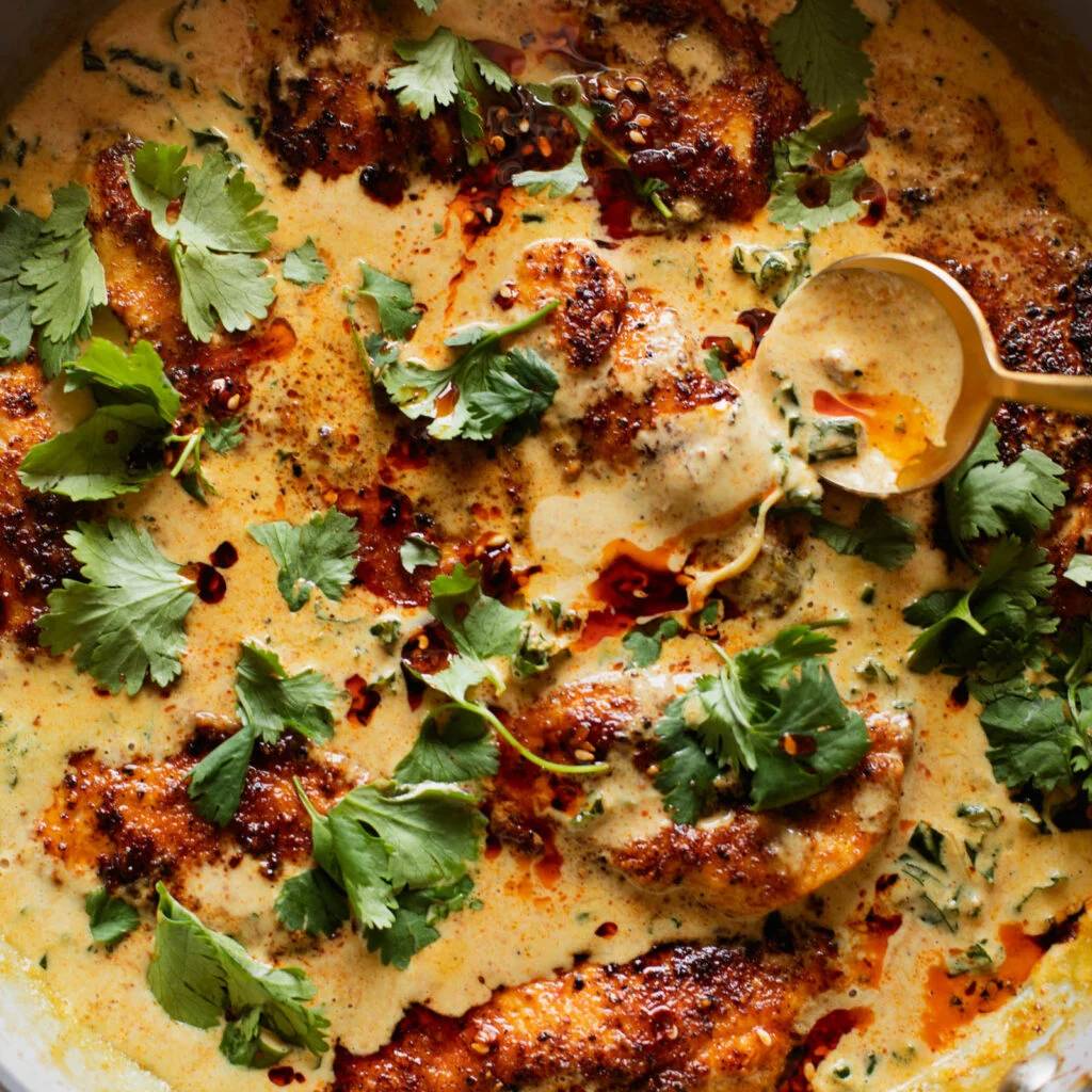 Chicken in a pan with coconut sauce and kale.