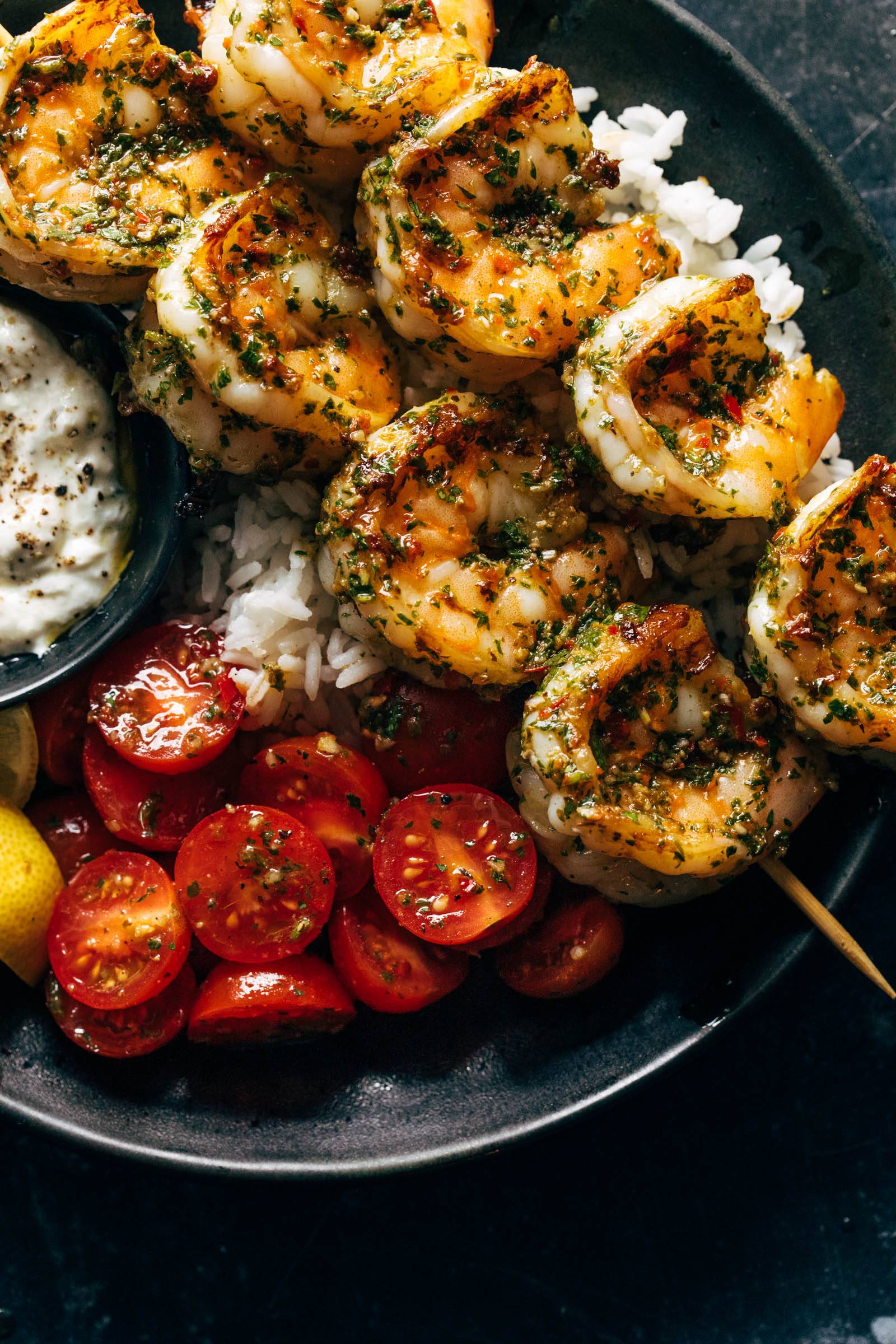 Shrimp on skewers, tomatoes, rice, and tzatziki on a plate.
