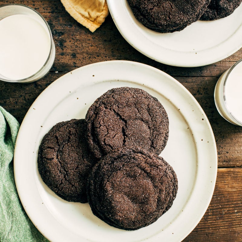 Dark chocolate cookies on a plate next to a glass of milk.