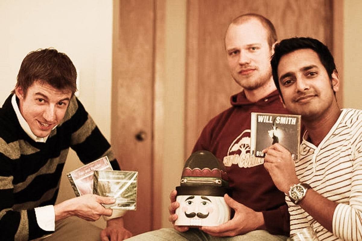 Three men posing for a photo holding cds and a figure of a head.