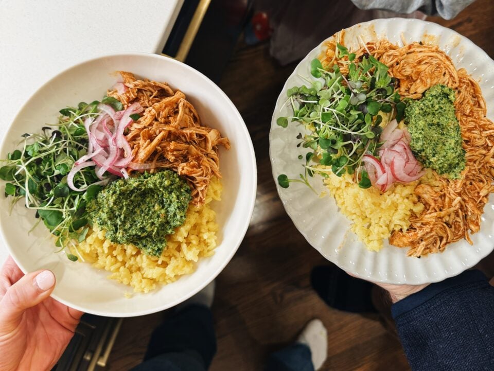 Two plates of crockpot chicken with rice, greens, and cilantro pesto.