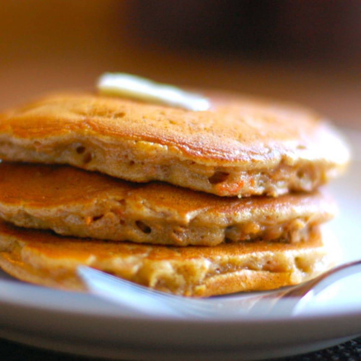 Cinnamon apple carrot pancakes with butter on a plate with a fork.