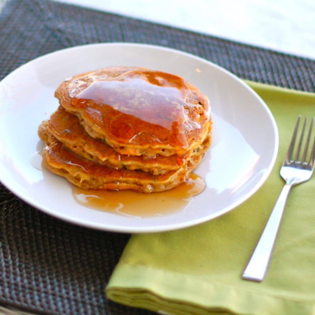 Cinnamon apple carrot pancakes on a white plate with a fork on a green napkin.