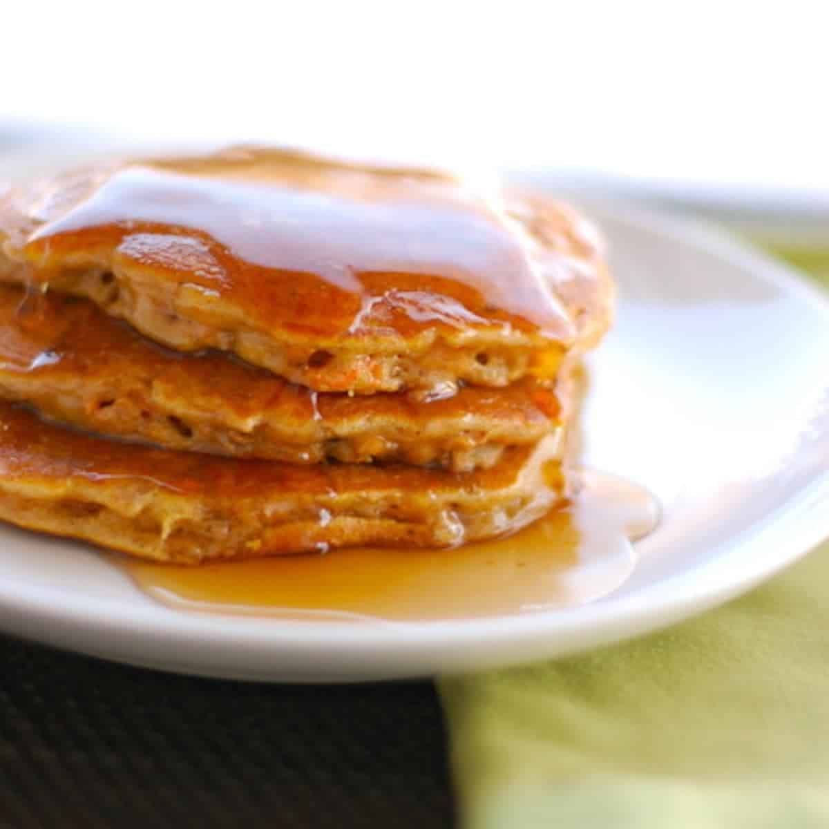 Cinnamon apple carrot pancakes with syrup drizzle on a white plate.