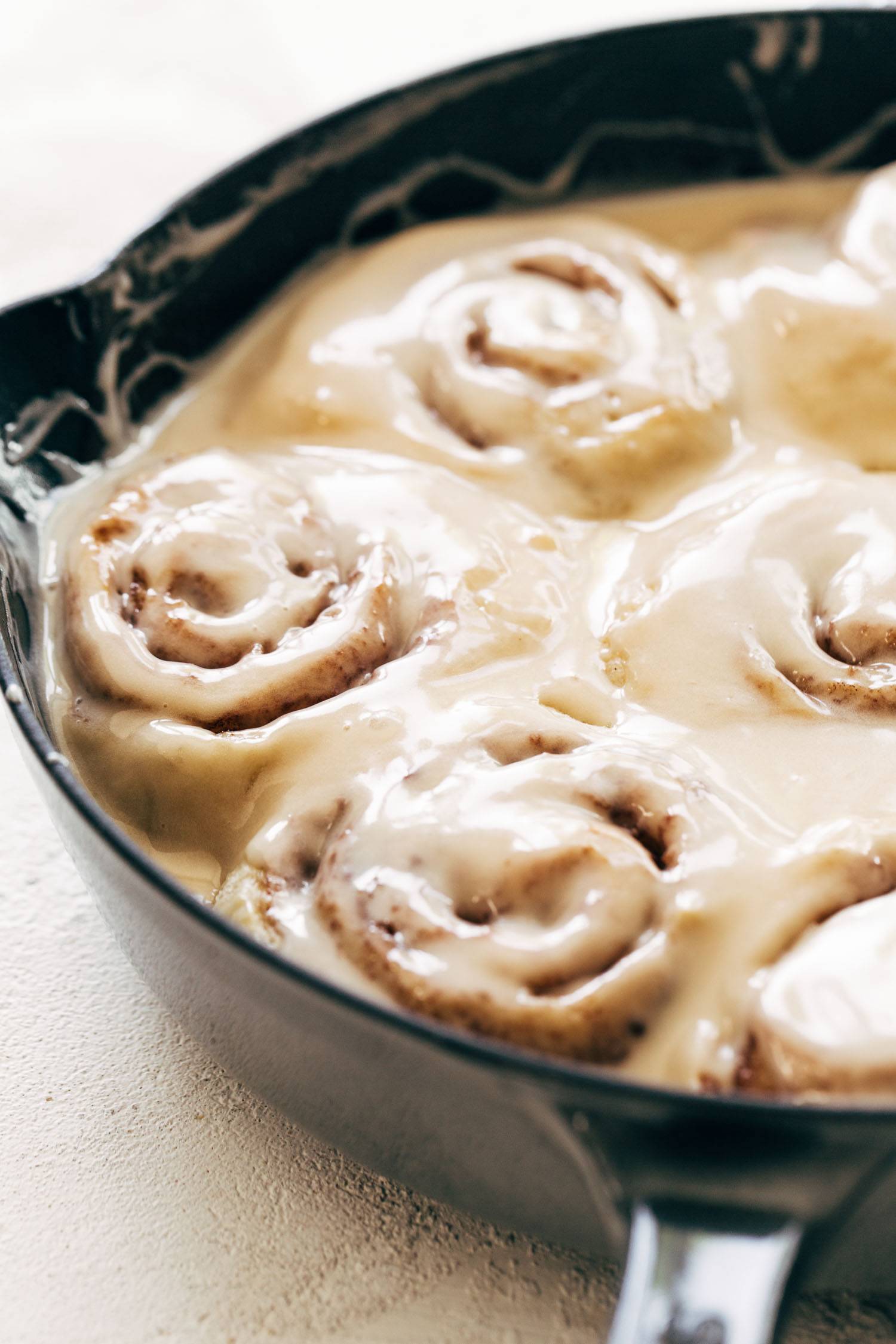 Cinnamon rolls covered with glaze in a cast iron skillet.