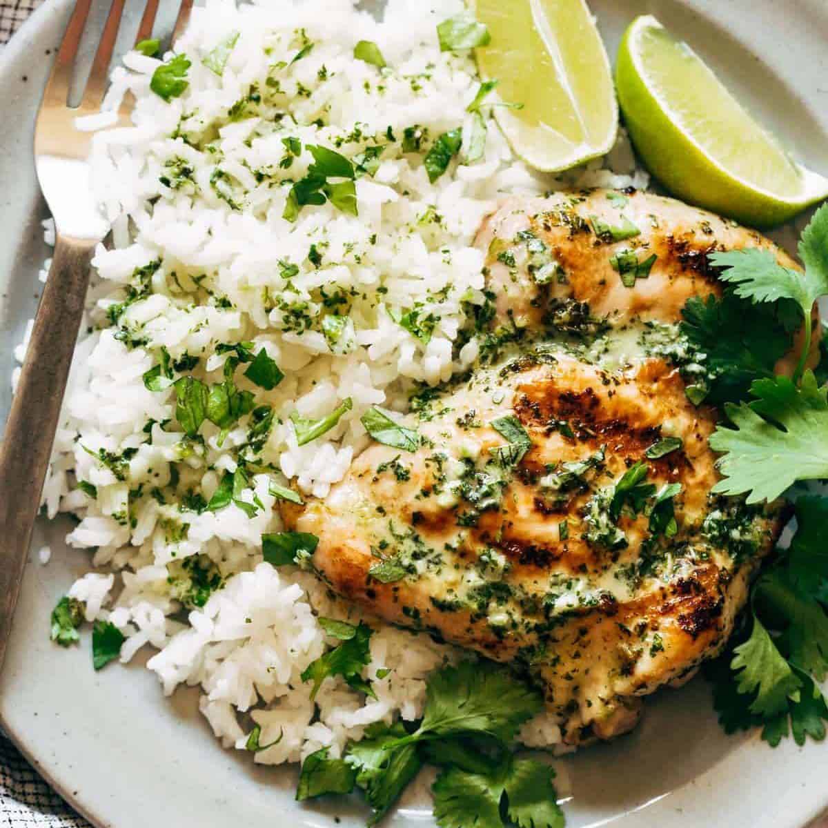 Grilled chicken on a plate with rice and lime wedges. 