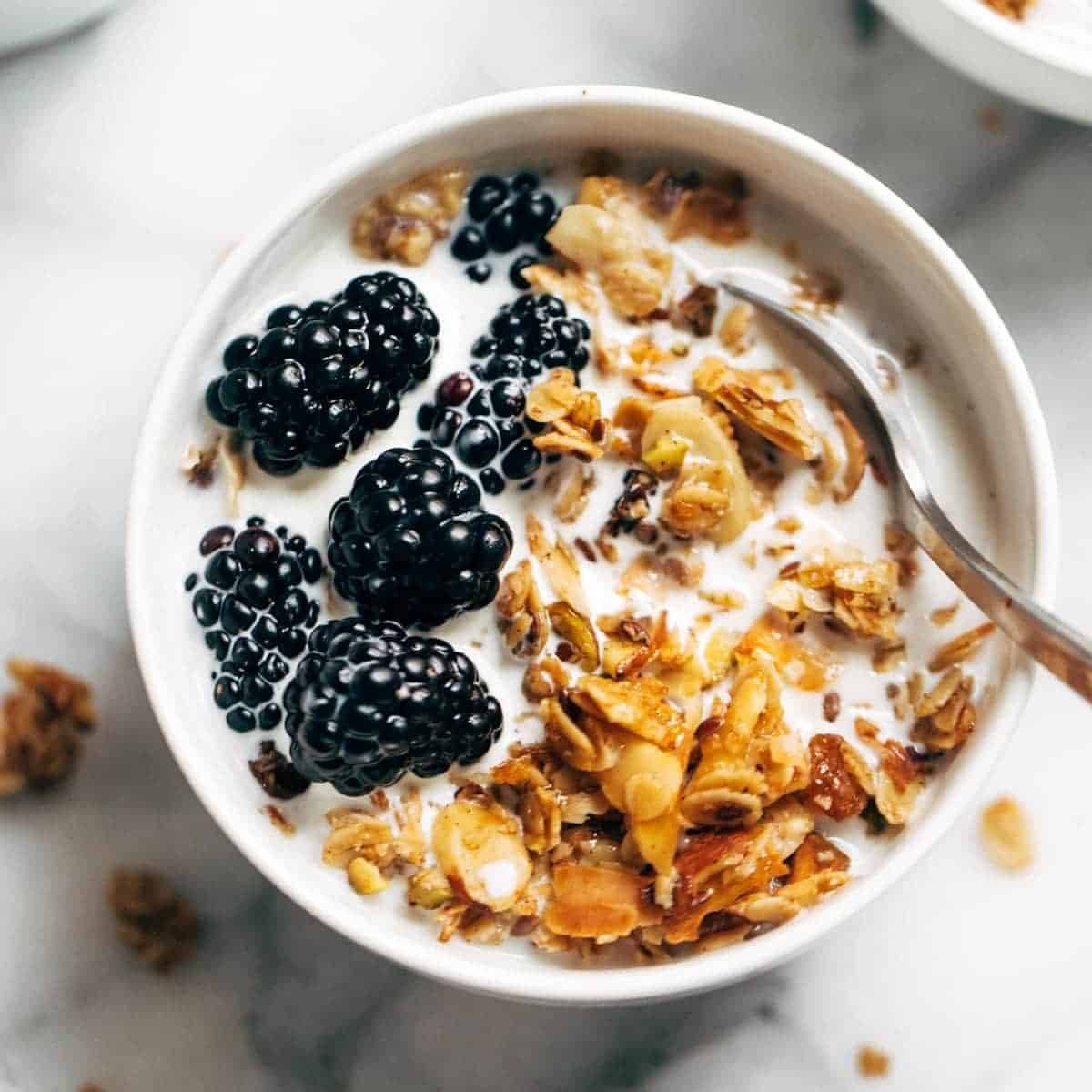 A bowl full of coconut oil granola and berries with a spoon in it.