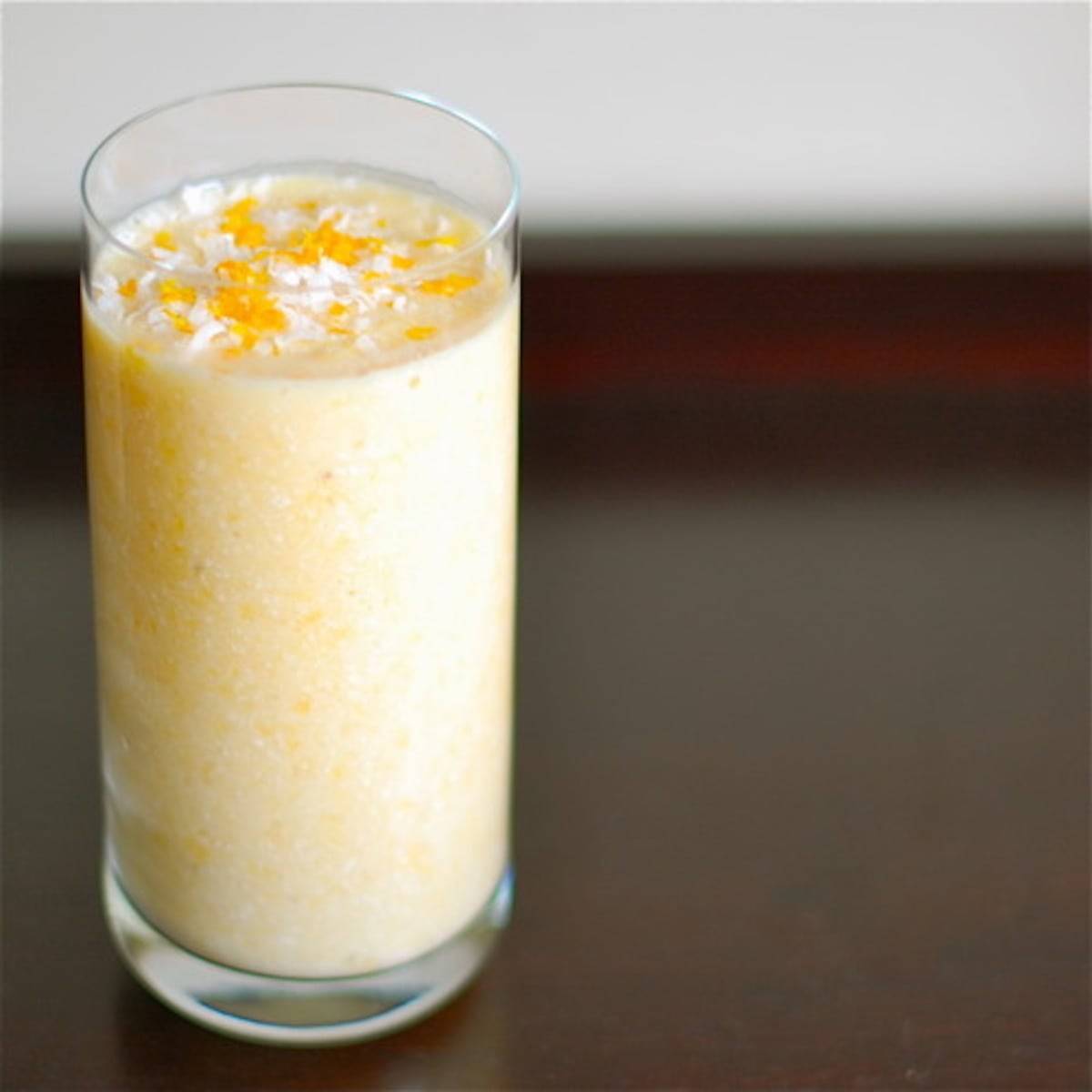 Coconut pineapple orange smoothie in a glass with fruit topping.