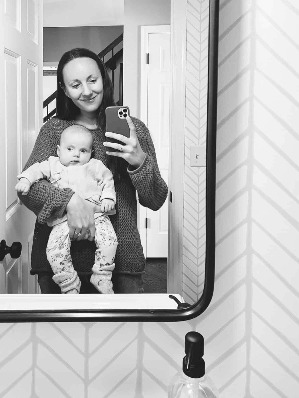 Lindsay holding her new baby taking a photo in the mirror.