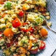 Quinoa with colorful diced peppers and tomatoes in a bowl with a spoon.