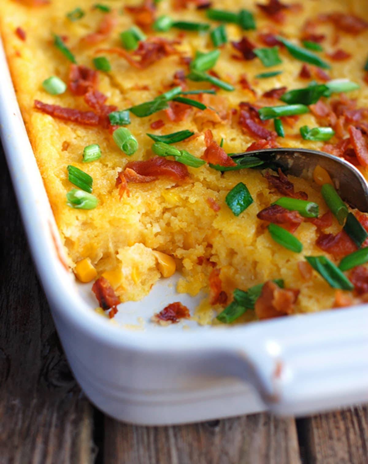 Creamy baked corn with a spoon in a white baking dish.