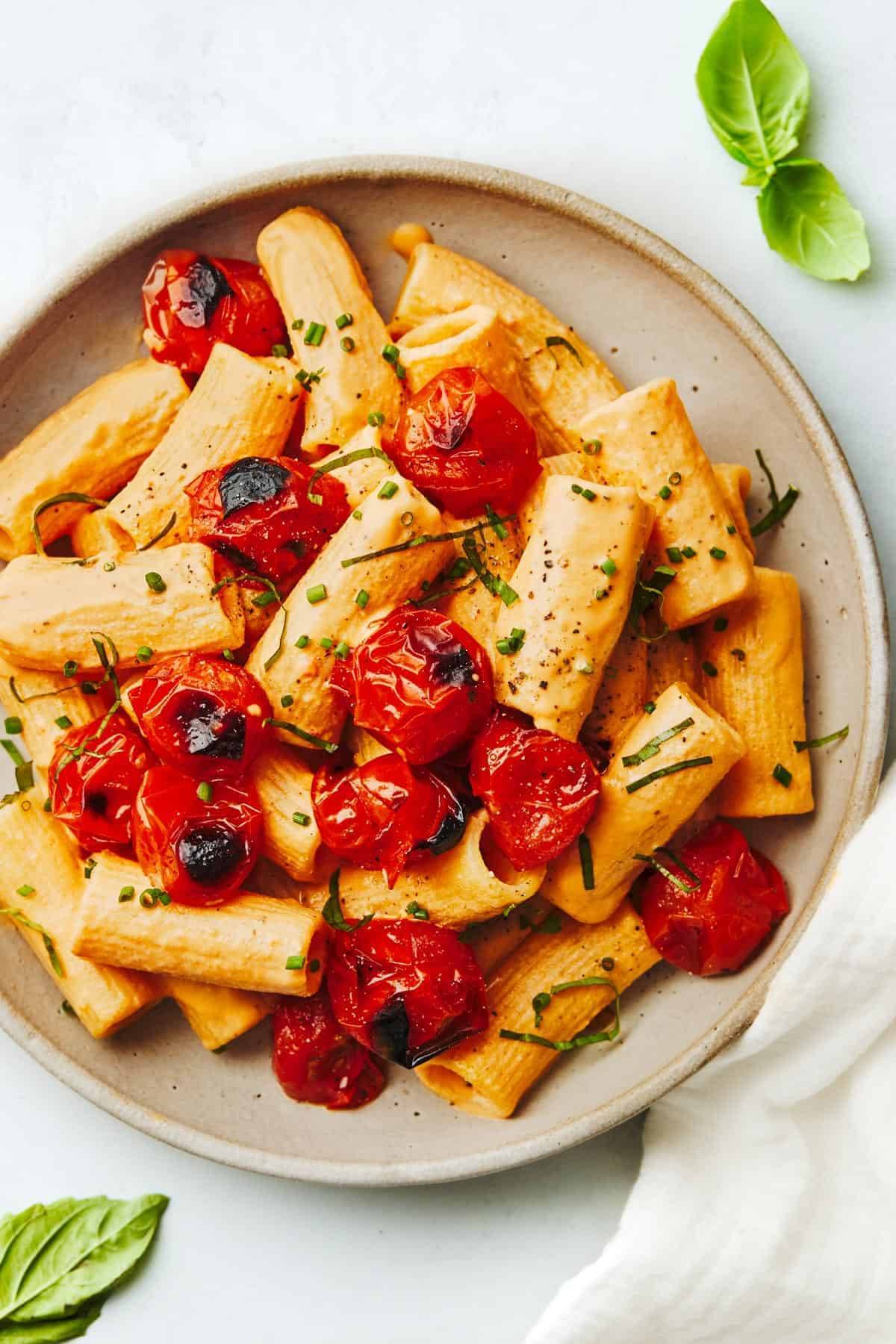 Creamy red pepper pasta on a plate with tomatoes.