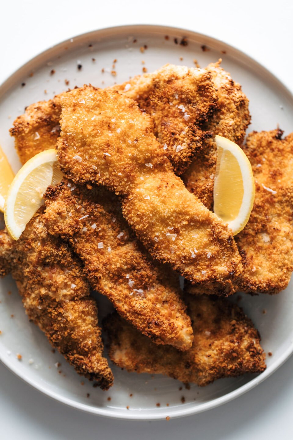 Crispy chicken cutlets on a plate with lemon wedges.