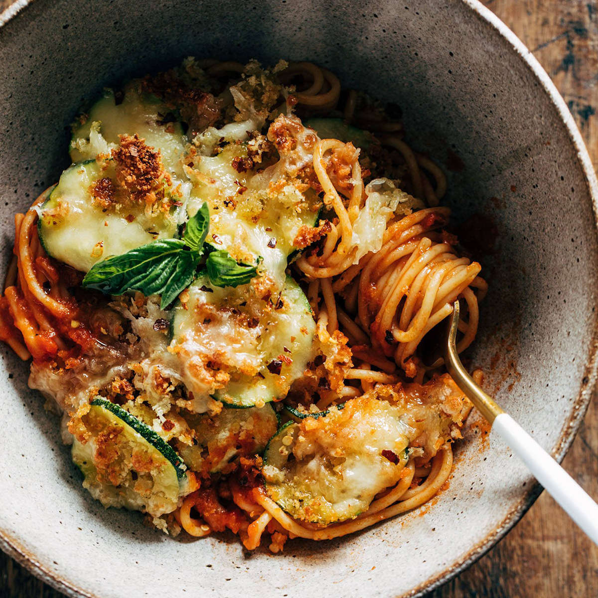 Spaghetti in a bowl with crispy cheesy zucchini on top.