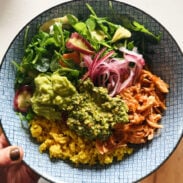 Crockpot chicken in a bowl with rice, greens, and cilantro pesto.