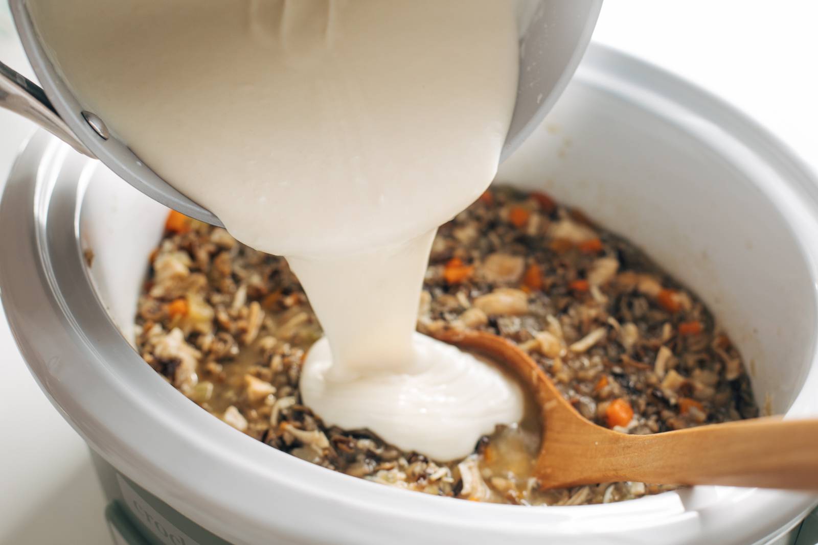 Pouring creamy mixture into a crockpot of chicken wild rice soup.