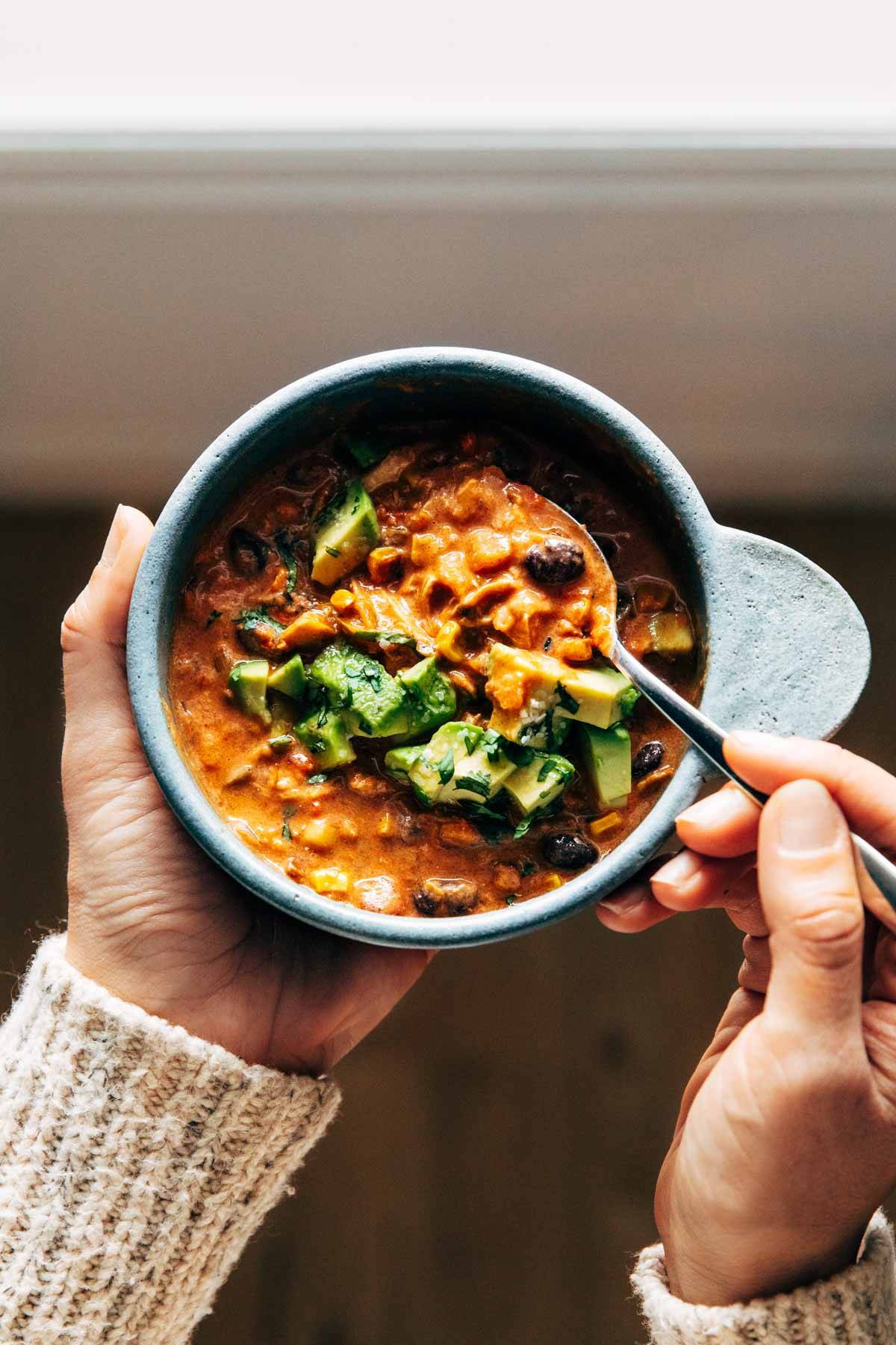 Queso chicken chili in a bowl with avocado and a spoon.
