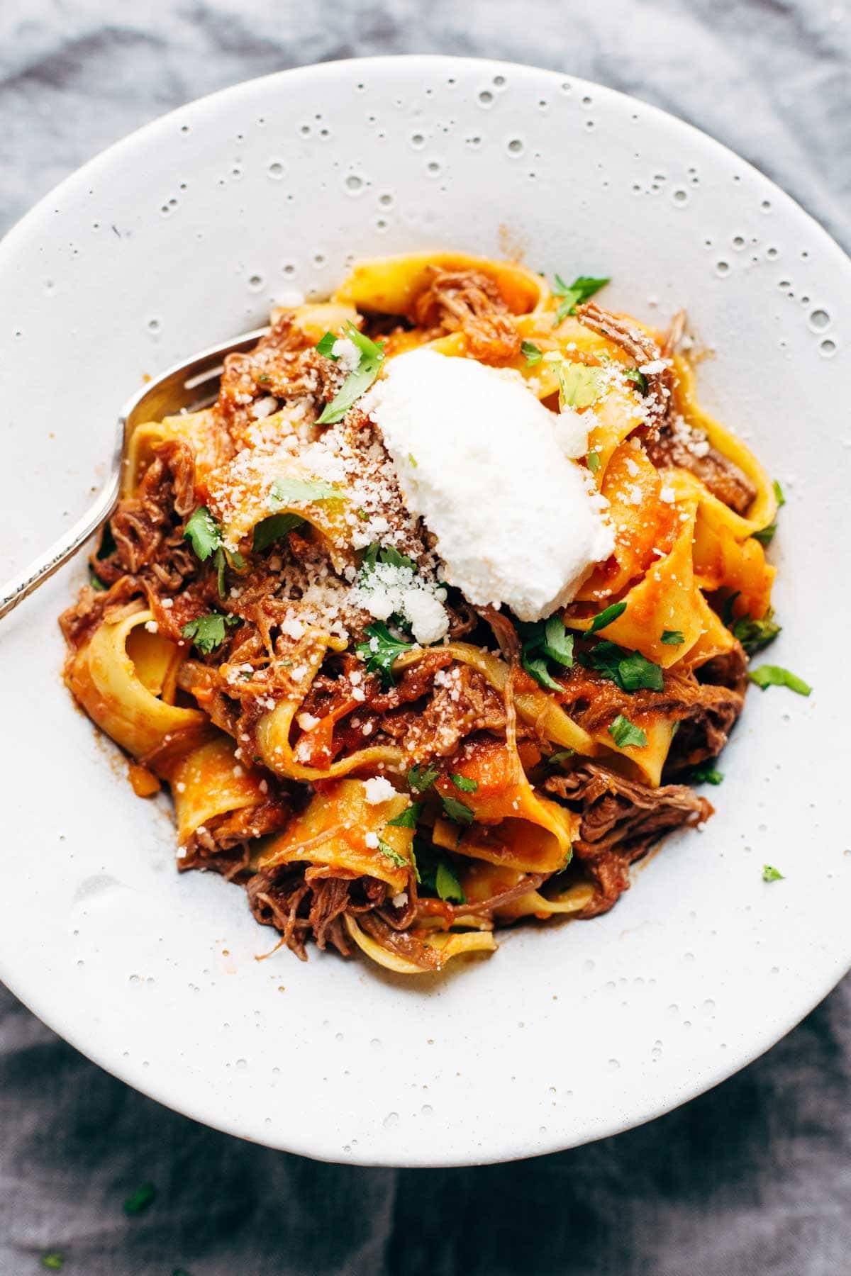 A big bowl of noodles with ragu and ricotta cheese.