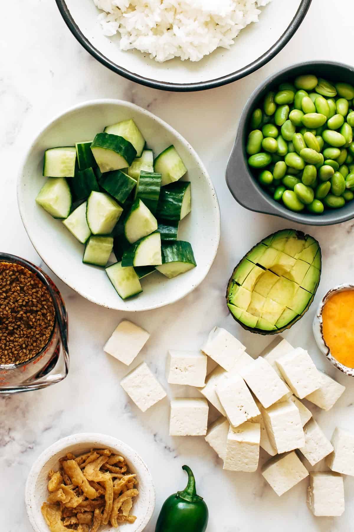 Ingredients in bowls for Crunchy Roll Bowls - rice, cucumber, edamame, tofu, avocado, sauce.