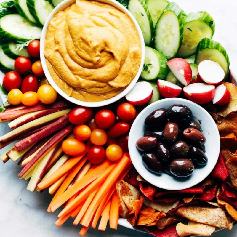 Plates of hummus and olives on a pile of vegetables.