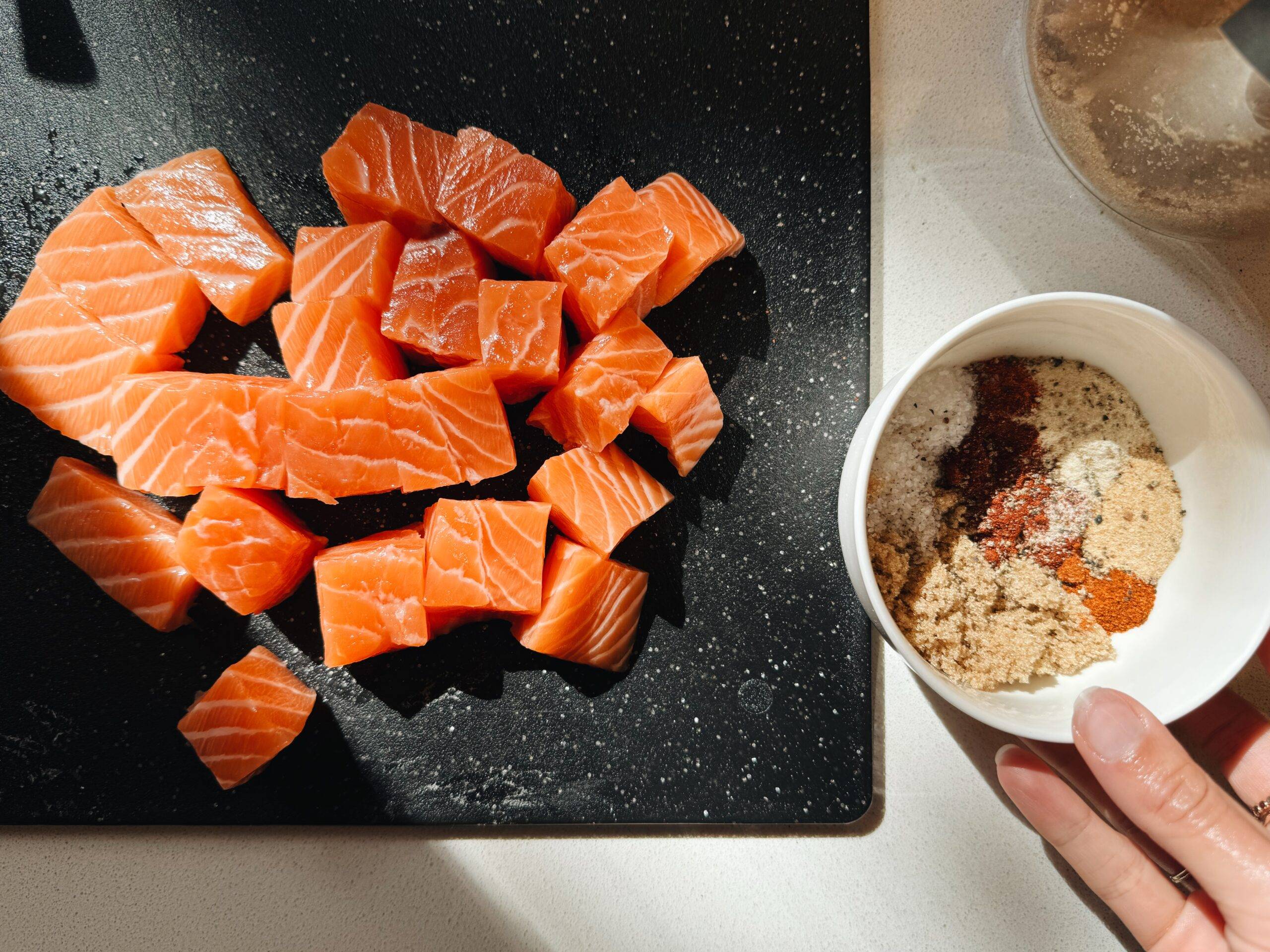Cubed salmon on a cutting board with a bowl of spices.