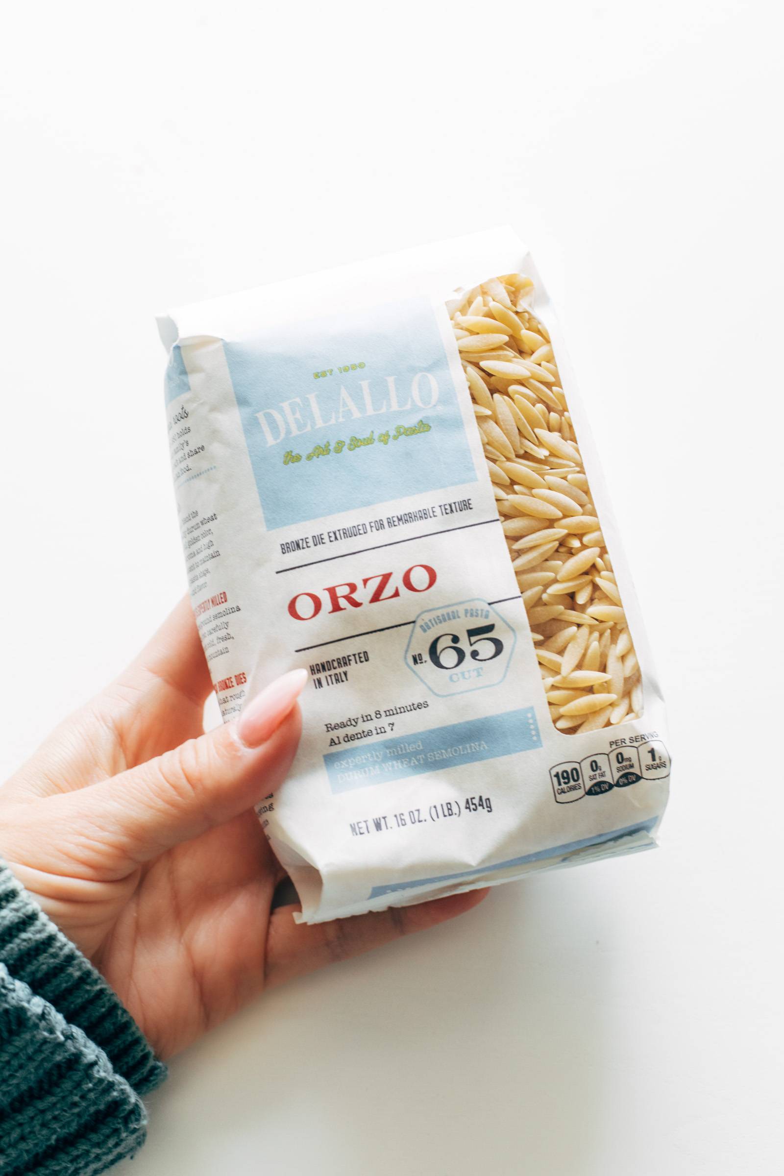 White hand holding a package of DeLallo orzo